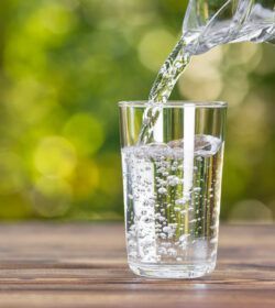 Water,From,Jug,Pouring,Into,Glass,On,Wooden,Table,Outdoors